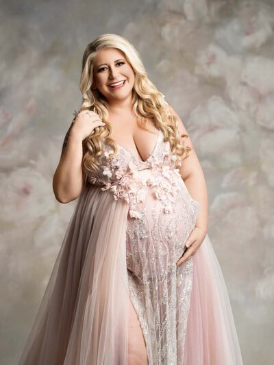 Feminine maternity portrait of blonde woman smiling wearing a pink gown with flowers