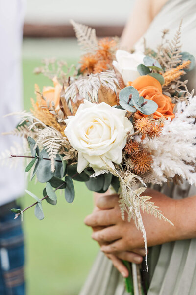 Close up photo of bridesmaid holding orange, cream and green bouquet.