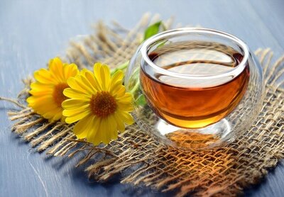 Tea in a small glass cup on burlap next to yellow flowers