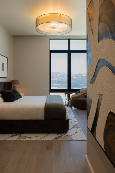 View through the hallway into a primary bedroom featuring a burlwood bed, brown velvet accent chair, and wrought iron side table, designed by Sister Studio.