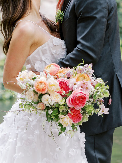 bride and groom stand together with closeup of lush pink and orange bridal bouquet and Casa dos Penedos in Sintra, Portugal