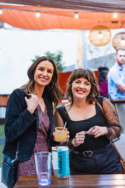 Two girls hold drinks and smile for Angela Marie Media at their corporate event.