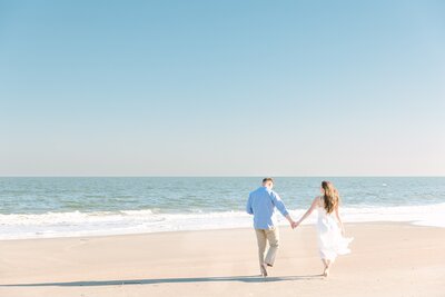 couple walk together holding hands toward the ocean