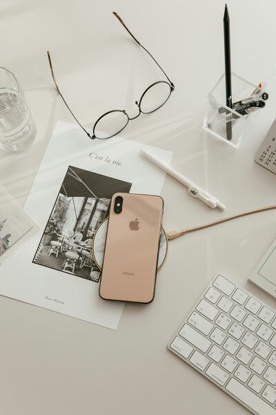 Overhead view of a tidy workspace featuring a smartphone, planner, glasses, pen, and keyboard on a white desk, representing productivity and organization.