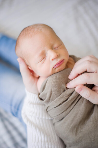 Newborn baby boy wrapped in a green swaddle asleep in Mom's hands