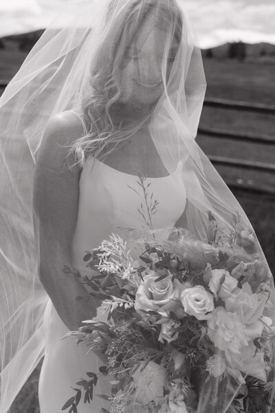 a bride while smiling with her veil over her head and holding flowers