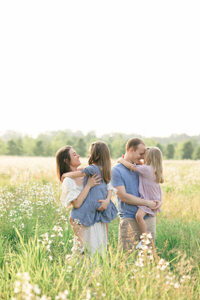 Family of four smiling and laughing as dad plays with the little girl in a field of flowers