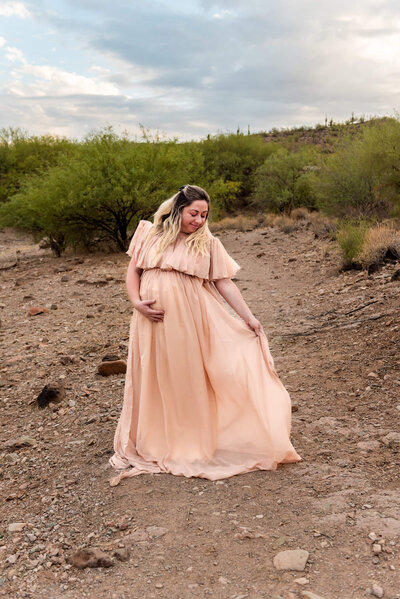 Expecting mother posing for maternity portrait in a blush colored dress. Taken by Cactus & Pine Photography