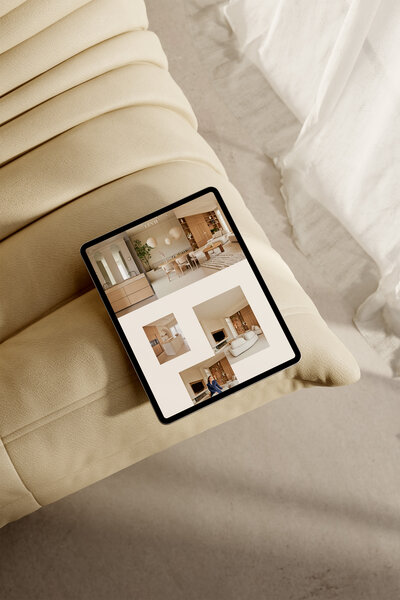 Tablet met portfolio van interieurstudio LEVH op een beige bank, met warme en minimalistische interieurontwerpen zichtbaar op het scherm