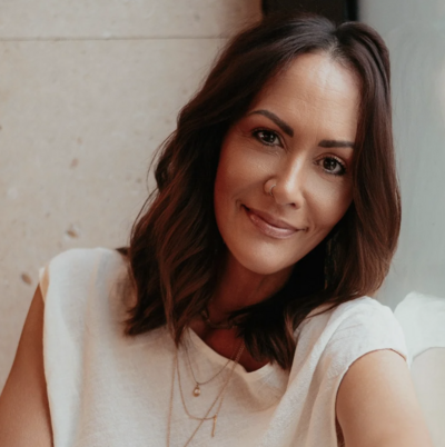 woman with brown hair gently smiling at the camera leaning against a window wearing an off white free people outfit