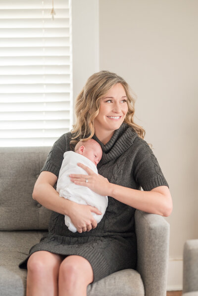 A mom holding her newborn baby on their home soda looking out the window
