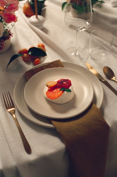 Softly lit film photo of a wedding tablescape featuring a modern place setting with gold flatware and a citrus-inspired dessert — a detail captured by a film wedding photographer.