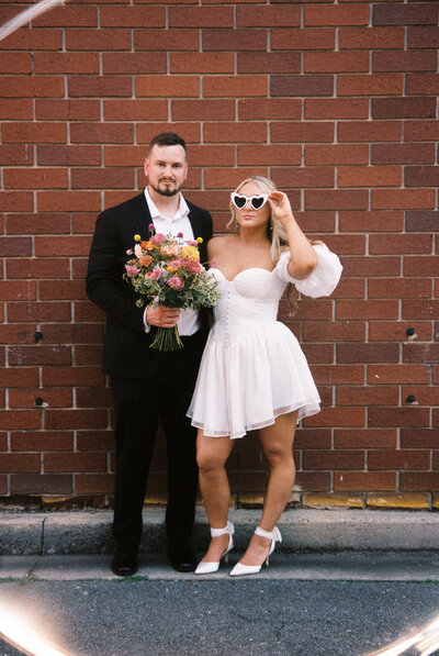 A couple poses in front of a brick wall