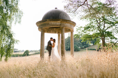 bride and groom in the grounds of delamere manor cheshire kissing underneath a victorian structure on their wedding day