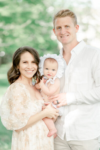 A mother and father smile as they hold their baby in a golden field by Nashville Newborn Photographer Kristie Lloyd