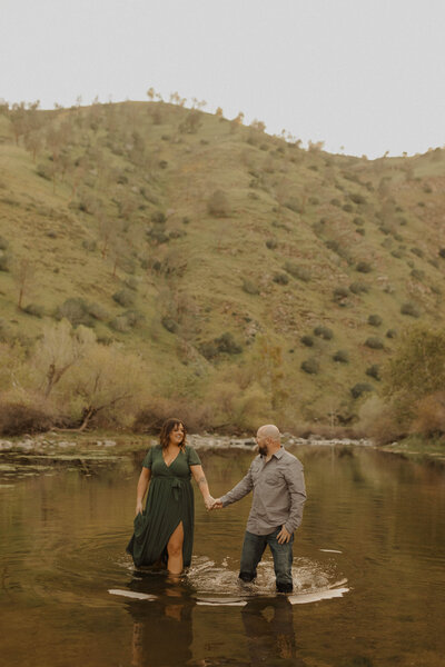 couple holding hands walking through a river