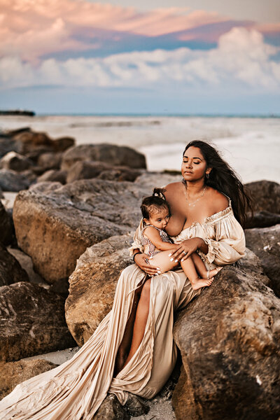 Family Photographer, a mother holds her baby boy near the ocean at sunset