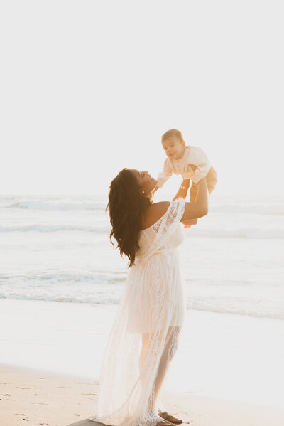 San Diego Family Photographer, woman lifting her little boy over her head near the ocean