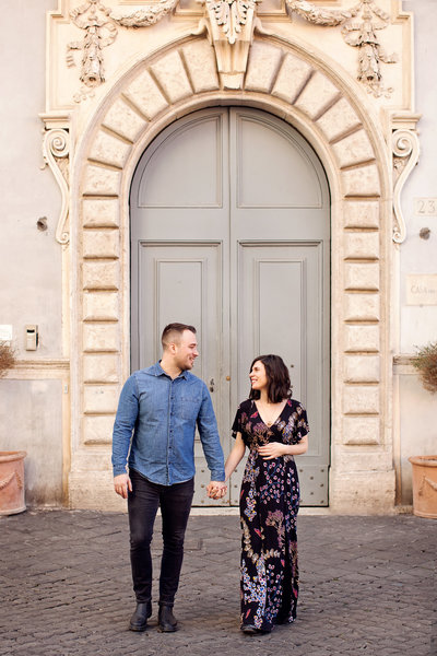 A couple on their babymoon standing in front of a blue and cream door in Trastevere. Taken by Rome Maternity Photographer, Tricia Anne Photography