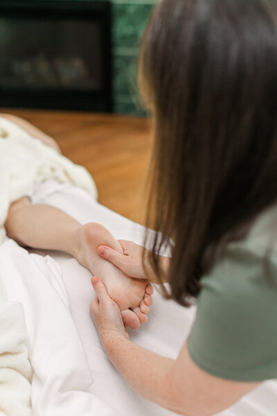Candice massaging the foot of a client as she lays on the massage table