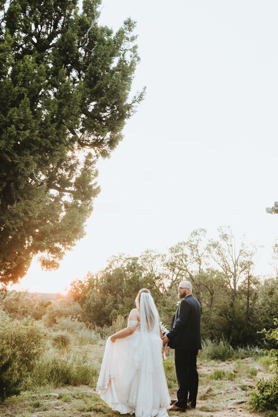 bride and groom walking hand in hand in a field
