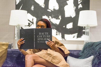 Tahirah sitting on couch holding a copy of "Haute Couture Ateliers"