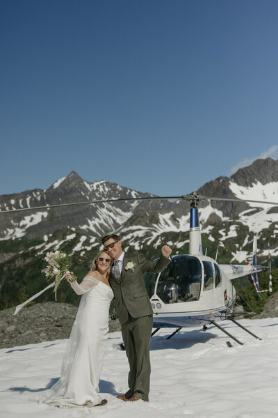 A couple standing in front of a helicopter in South Central Alaska. 