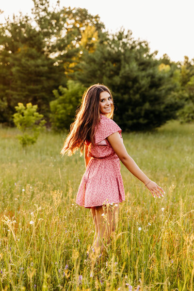 high schooler in a pink romper spinning in a field at sunset for her senior photos.