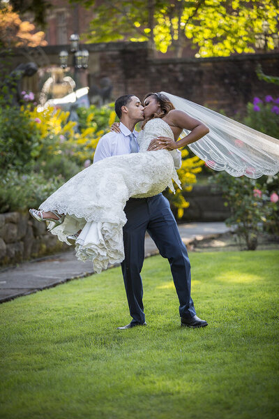 Groom holding bride in arms and kissing her in garden