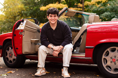 Casual senior pictures of smiling young man in black against his bright red sports car in Pittsburgh pa.