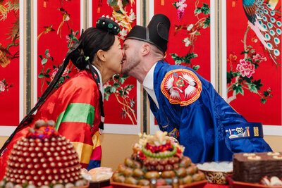 Man and woman in traditional Asian wedding garb kissing each other
