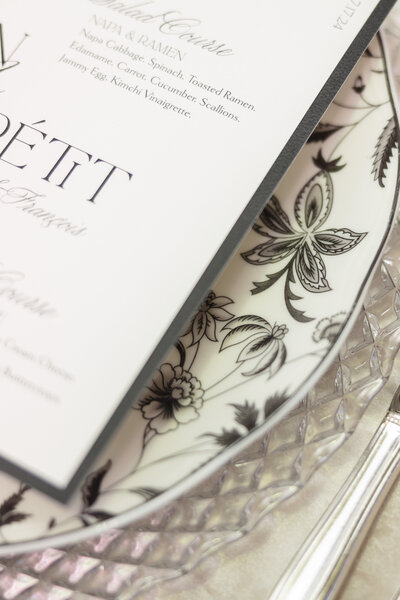 Close up of a wedding table setting decorative black and white floral plate with white stationery overlay. 