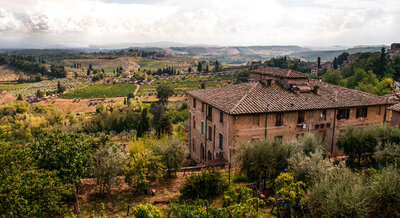 Old stone villa overlooking rolling vineyards, olive trees, and farmland in the Tuscan countryside.