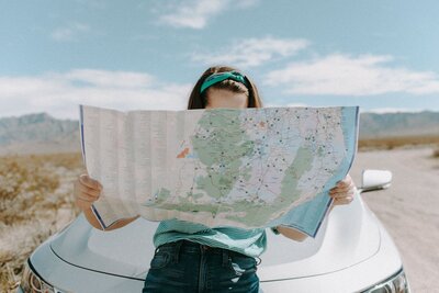 Woman leaning on the front of her car looking at  a printed road may  spread in her hands