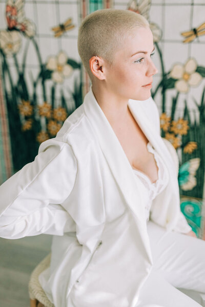 Woman with blonde hair buzz cut in all white outfit looking away from the camera