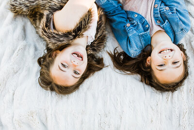 two adolescent sisters lay on blanket laughing and looking up towards the sky