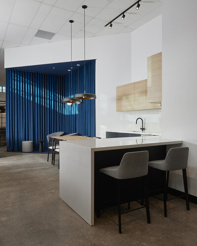 A kitchenette seating area featuring multiple chairs, a sink, wood cabinetry, modern lighting fixtures, and a decorative deep blue curtain