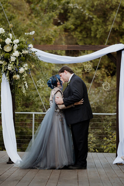 Couple shares a kiss beneath a floral wedding arch during a romantic outdoor Wimberley wedding planned with creative flair and care.