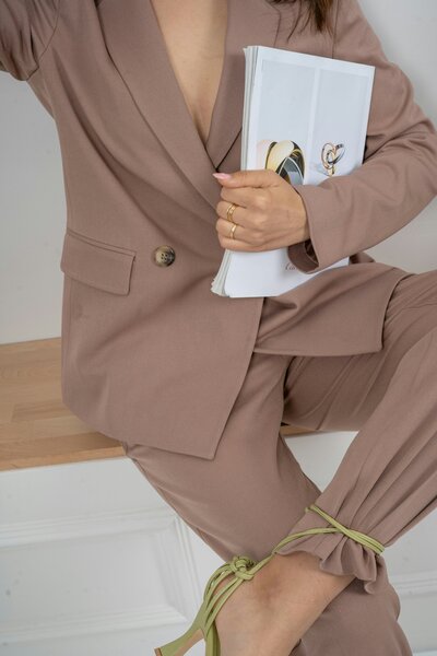 a woman sitting on a bench with her leg crossed wearing a mauve suit and holding a stack of papers. 