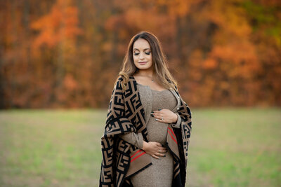 Pregnant woman cradling her belly for her Burlington outdoor fall maternity photos 