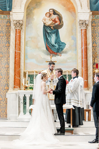 a bride and groom holding hands in a church during a Catholic wedding ceremony