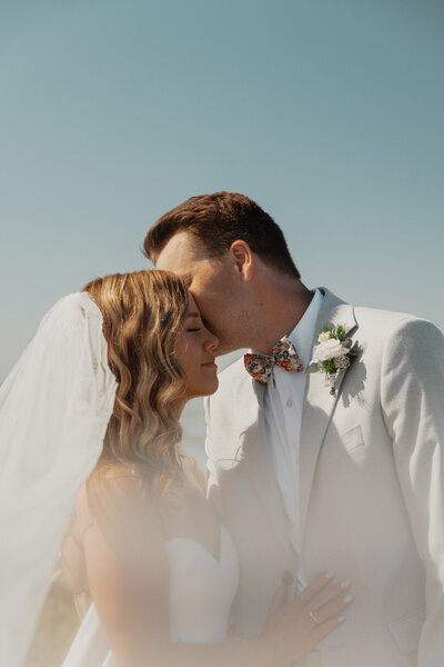 Groom kissing the cheek of his new bride during wedding portraits in Comox by Latitude 49 Photography
