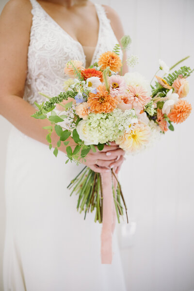 Bride holding her bouquet full of greenery and pink and yellow colors.