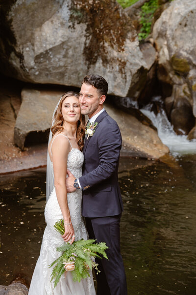 A couple poses in front of a waterfall at their Yosemite elopement