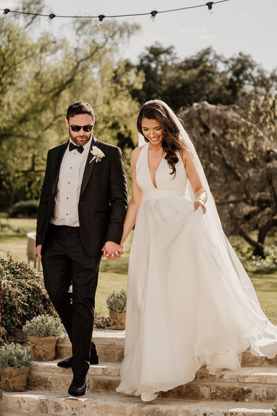 Groom wearing sunglasses and holding brides hand on outdoor steps