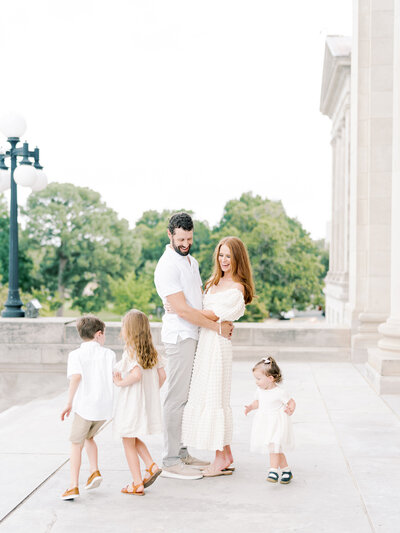 Mother and father embrace while their 3 children run silly circles around them