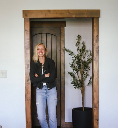 Interior designer Kaitlyn Schultz standing in a rustic doorway, welcoming clients to KSC Interiors in Northern Colorado.