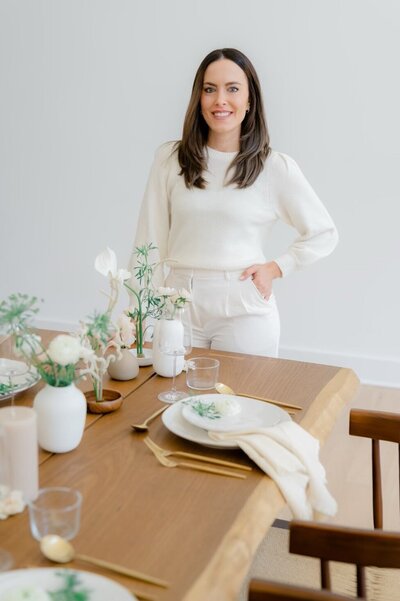 A woman dressed in white standing next to a table.