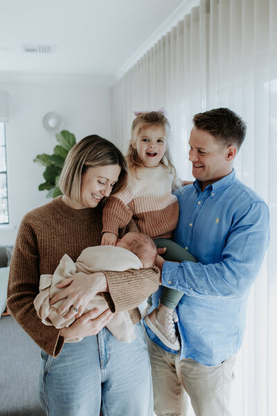 A couple smiles as they look down at their yawning newborn