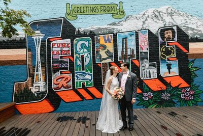 Couple standing of an artistic Seattle mural smiling at each other.